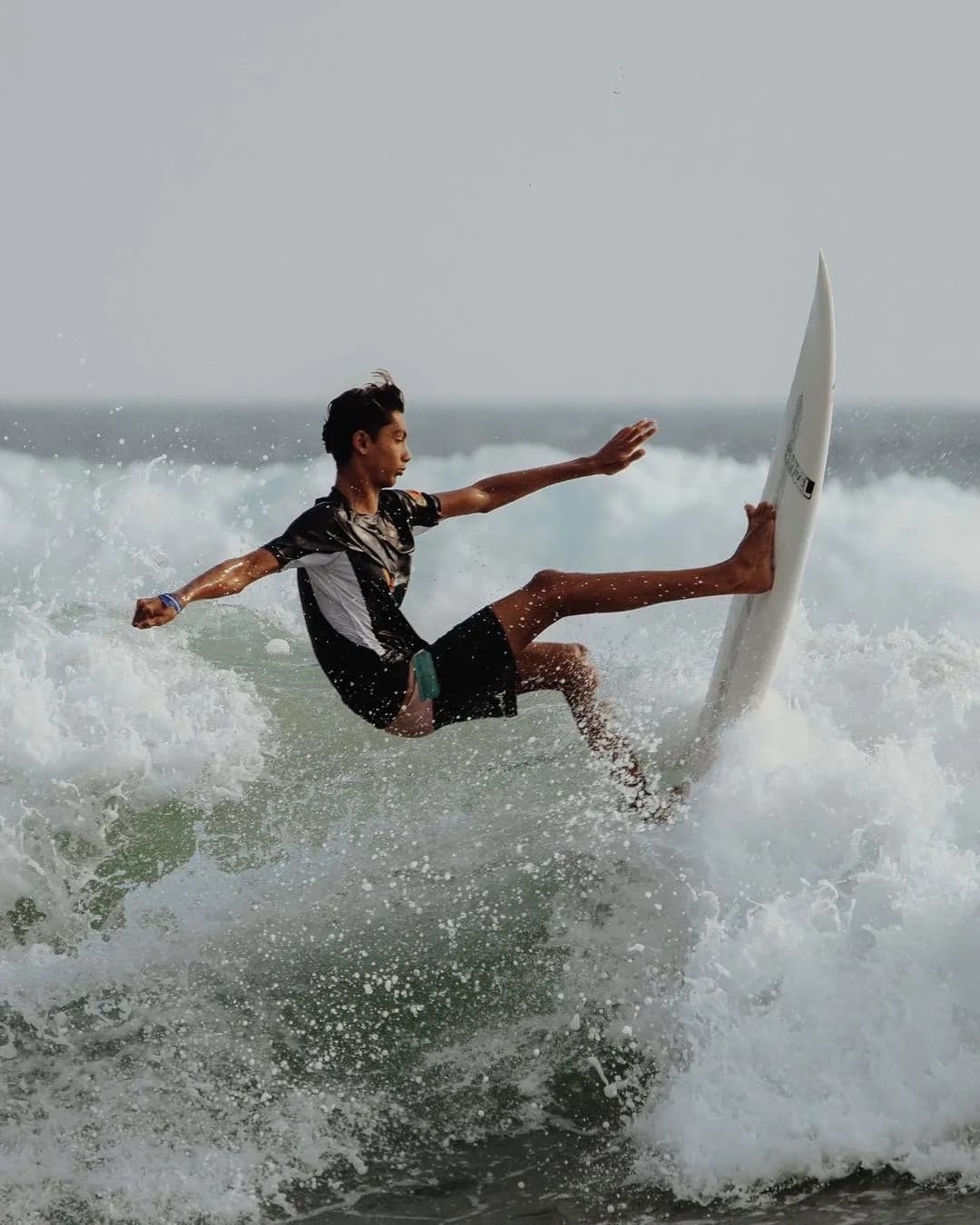 Surfer riding a wave at Dewata Beach in Sri Lanka, with the sun setting in the background and palm trees lining the shore.